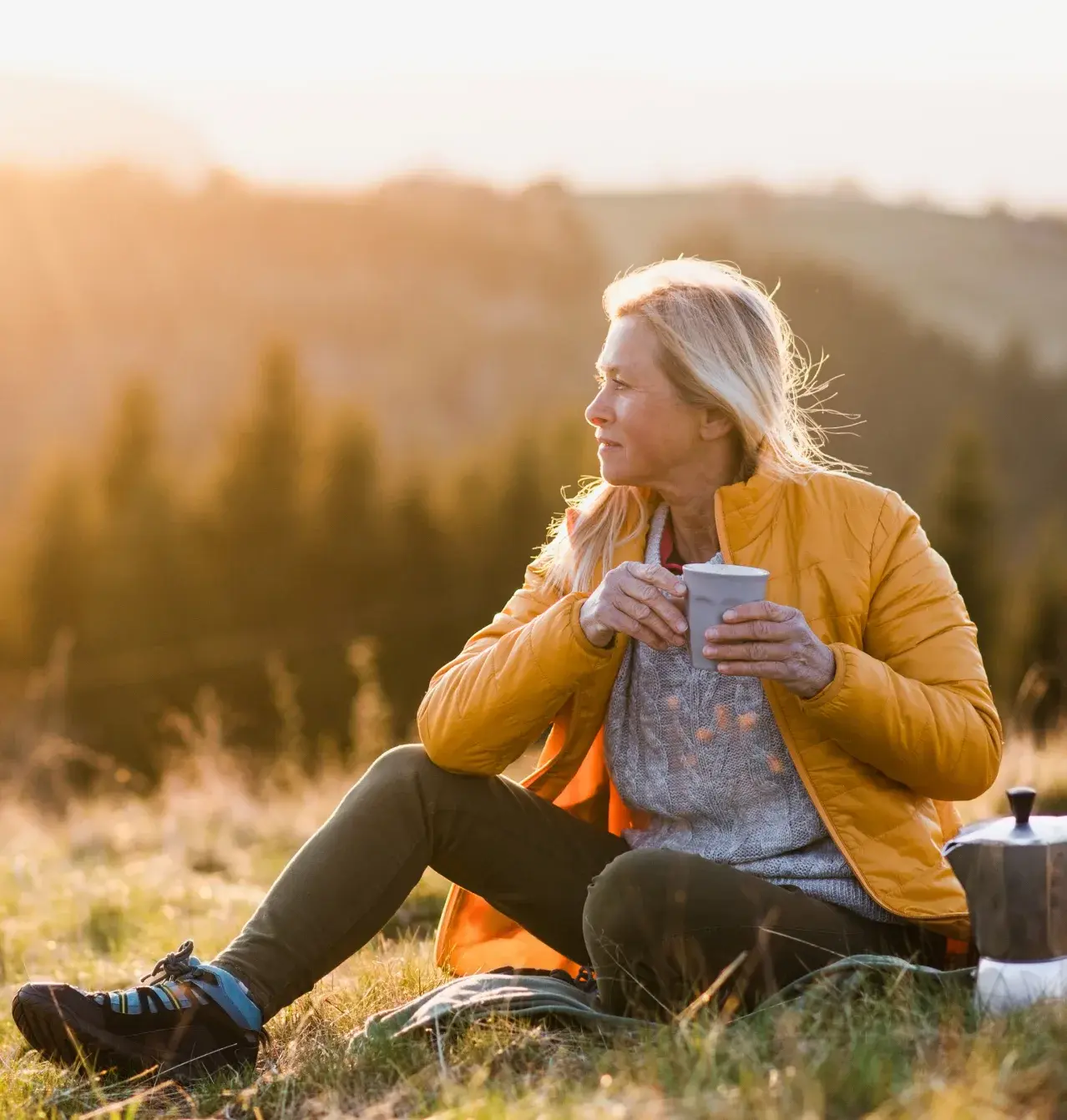 Woman sitting outdoors at sunset holding a mug